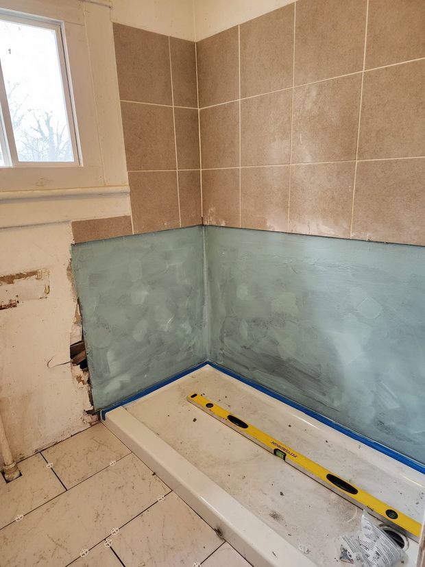 Partially tiled bathroom wall under renovation with blue waterproofing and a shower tray below