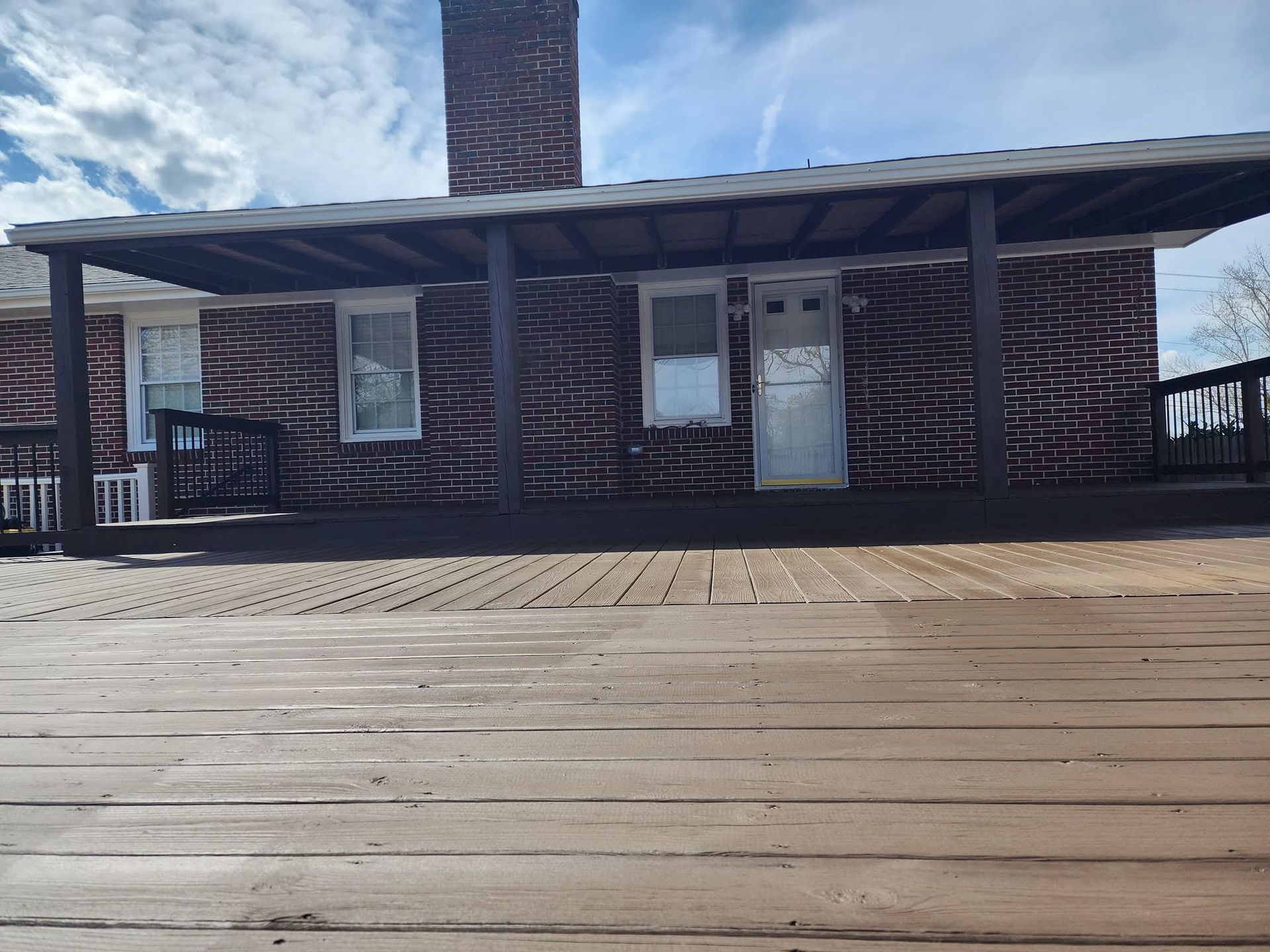 Brick house with covered porch and white door behind a wooden deck under a blue sky