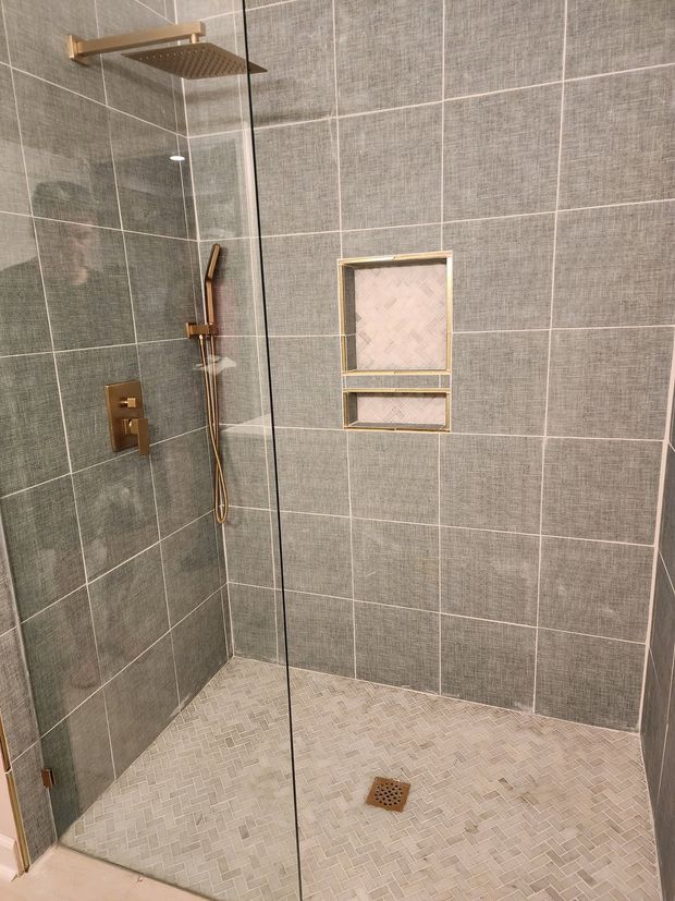 Tiled shower stall with built-in shelves, a small window, and a drain on the floor.