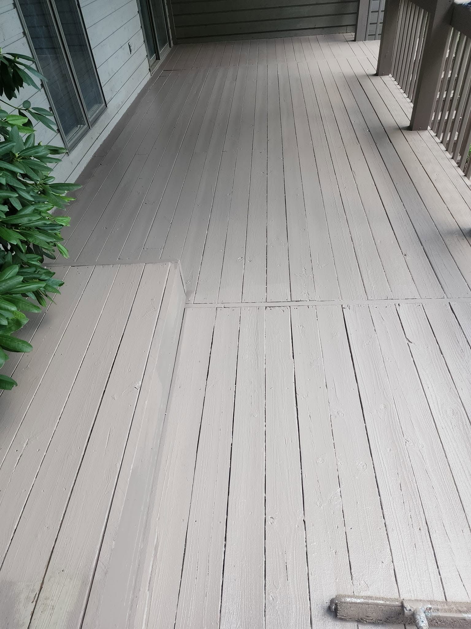 Covered outdoor walkway with light wood decking and plants along the left side.