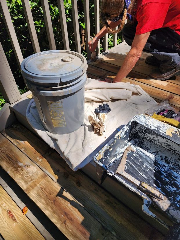 Paint buckets, tools, and a person working on a sunlit wooden deck project