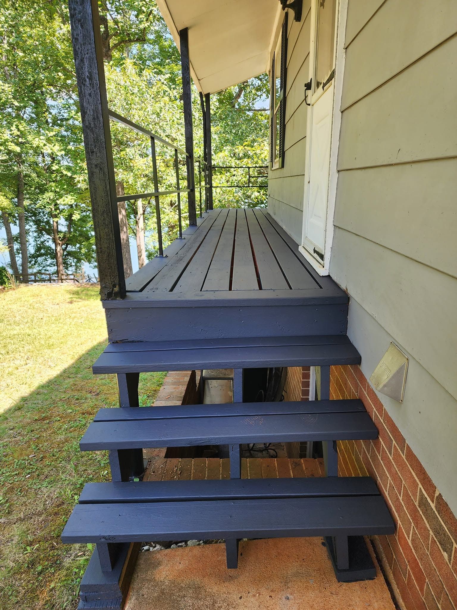 Black wooden porch steps leading to a small front deck beside a yellow house and wooded yard