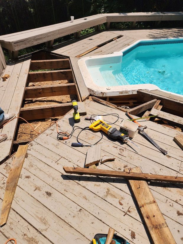 Damaged wooden pool deck with tools and broken boards beside a turquoise swimming pool