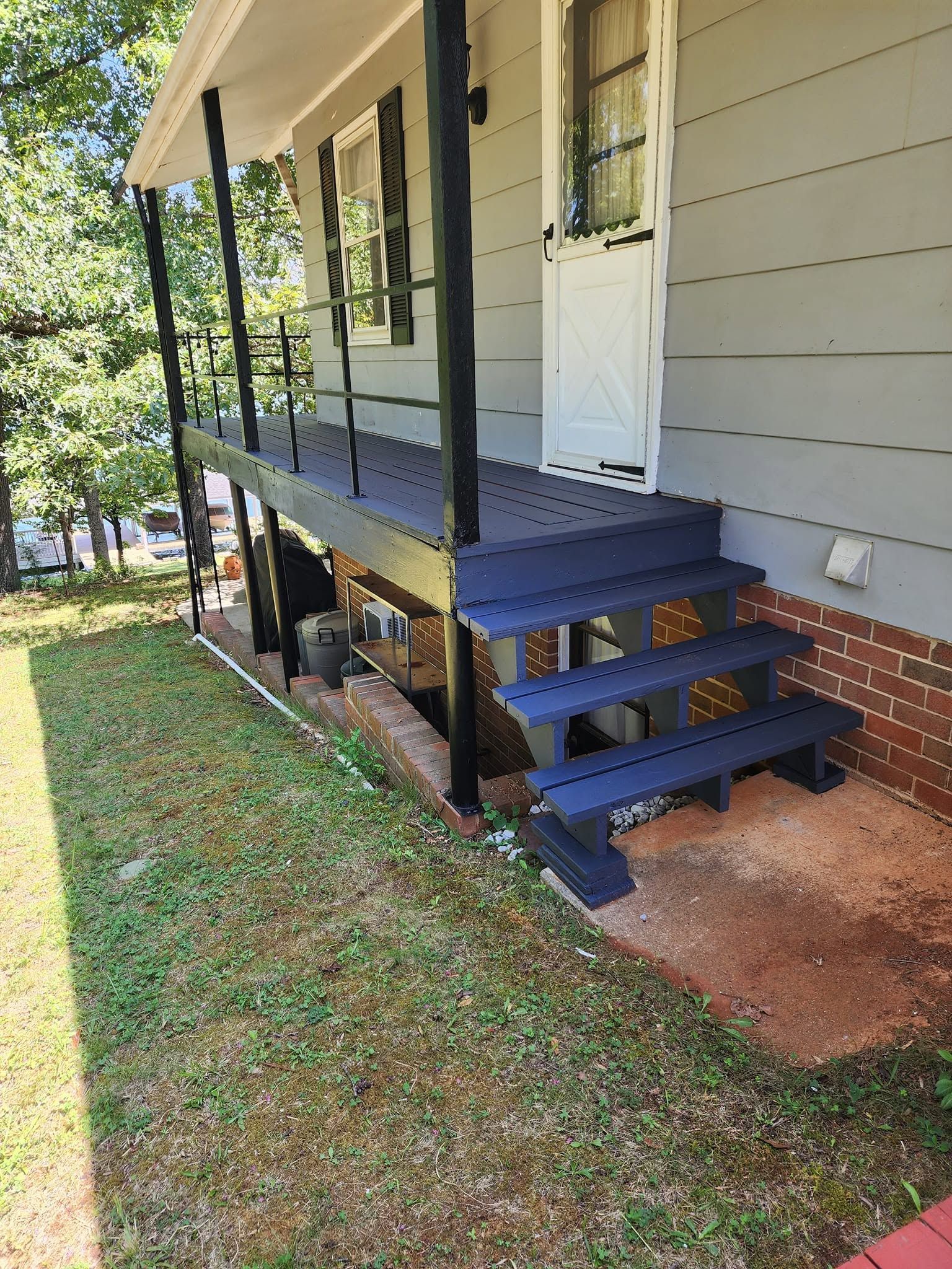 Small porch deck with blue steps, white door, and railing on a house with a grassy yard