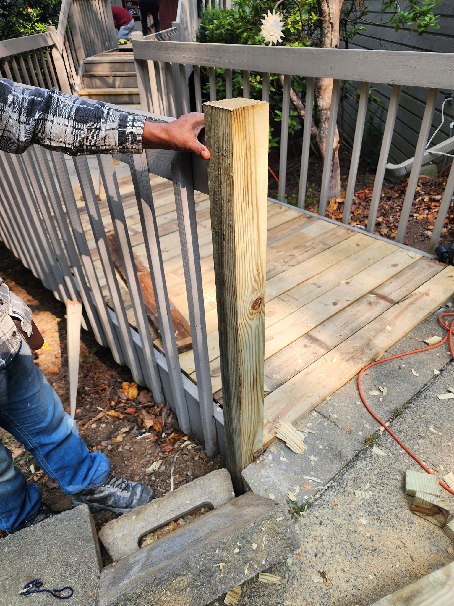Person installing a wooden post beside a deck railing outdoors