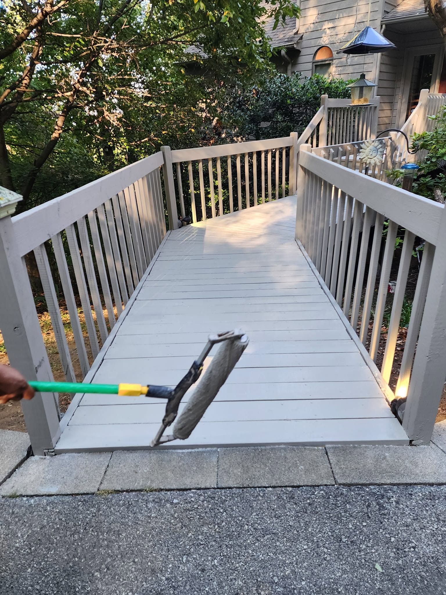 Person mopping a wooden ramp with white railings outdoors.