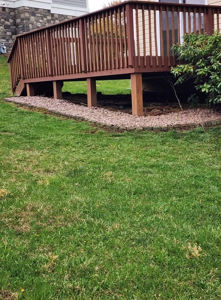 Wooden deck with railing elevated over a grassy yard, with a gravel border underneath