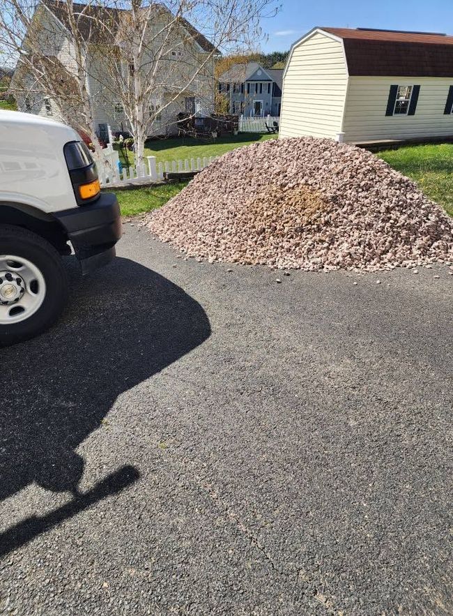 Driveway with a large pile of mulch or gravel beside a white van in a suburban yard