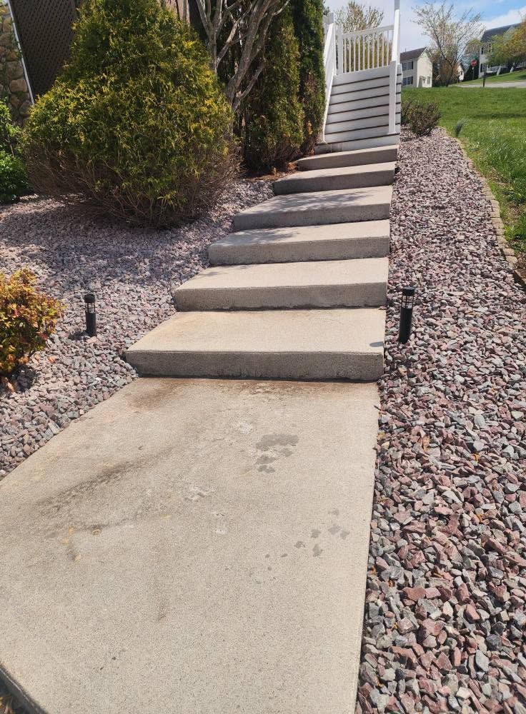 Concrete steps leading up a landscaped front yard beside gravel and shrubs
