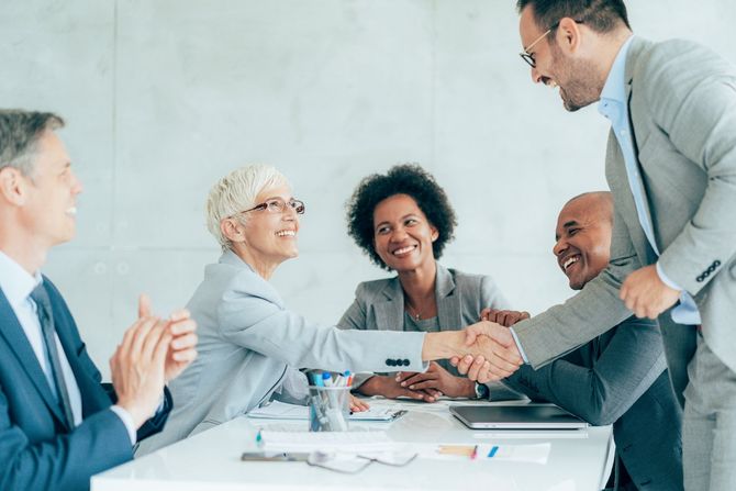 A group of business people are sitting around a table shaking hands.