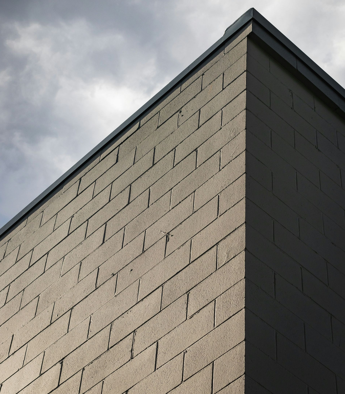 Brick building corner with a dark roof against a cloudy sky