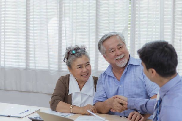 Smiling elderly couple shaking hands with financial advisor at a table.