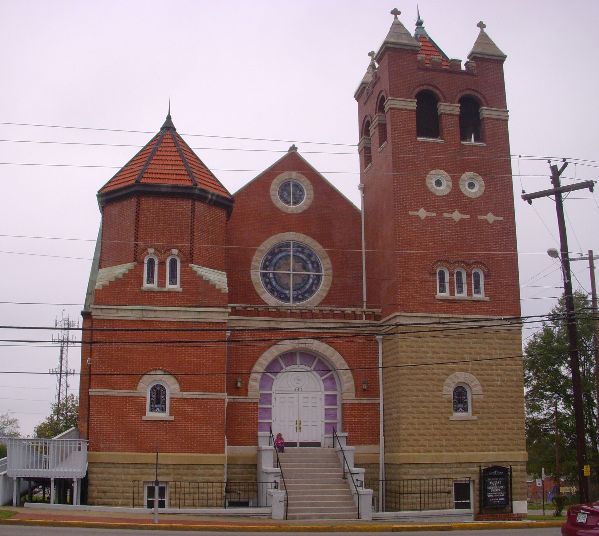 Old red-brick church with twin towers, circular stained-glass windows, and front steps under a gray sky