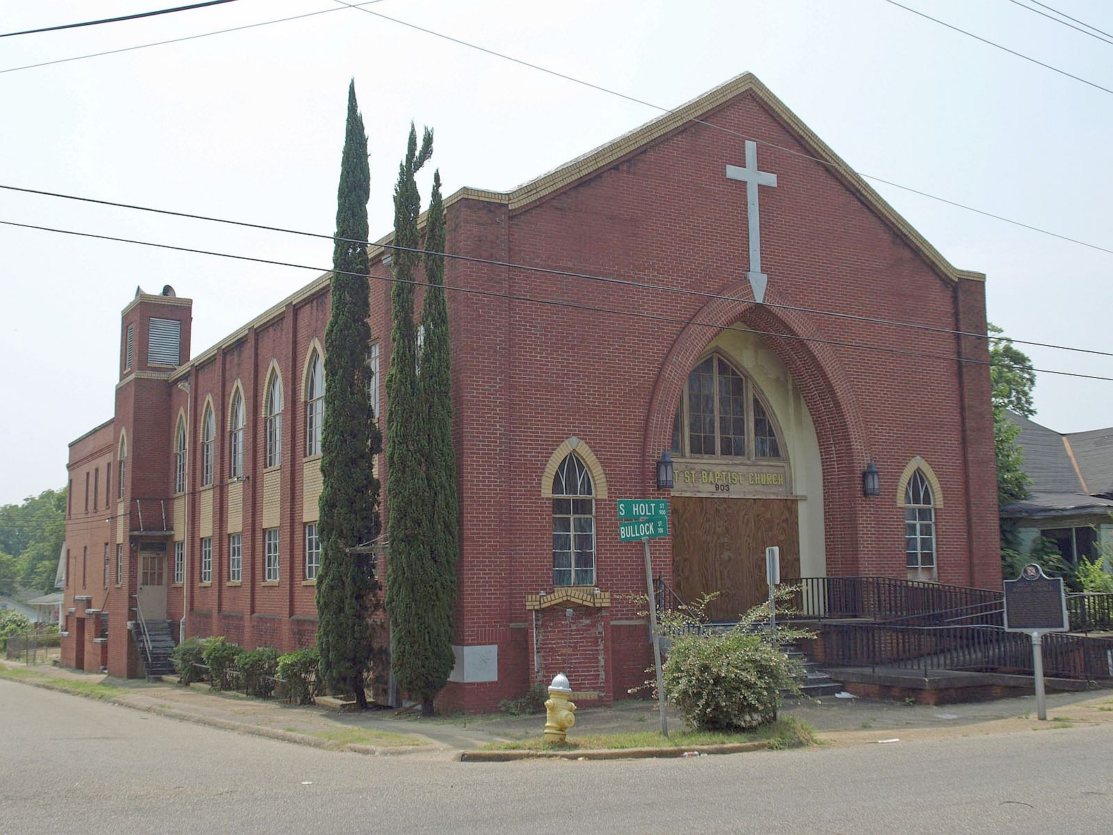 Red brick church with tall cross and arched entrance on a street corner