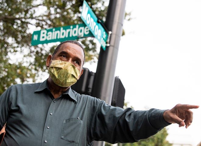 Masked man pointing at a street sign on a city corner