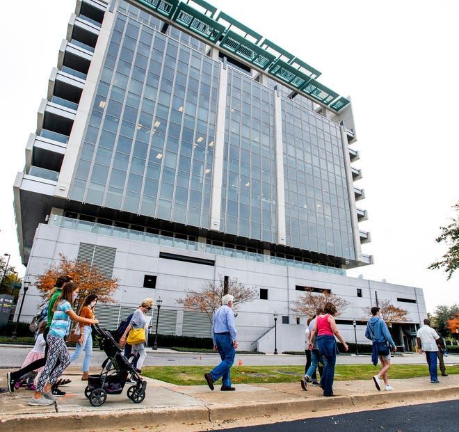 People walking past a tall glass office building on a sidewalk.
