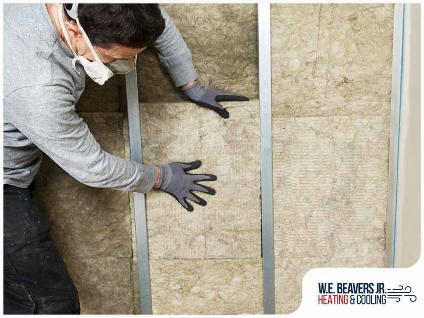 A man wearing a mask and gloves is insulating a wall.
