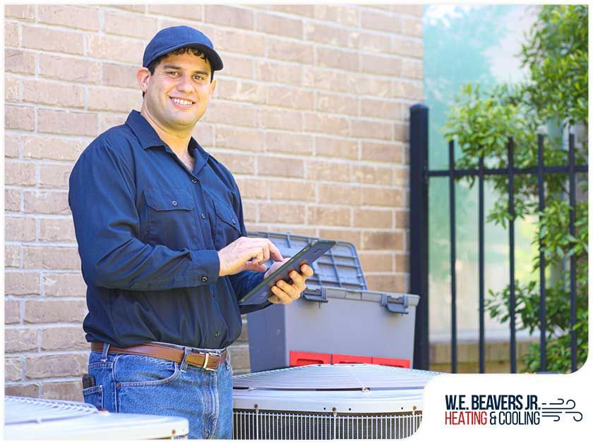 A man is standing in front of a brick building holding a tablet and a toolbox.