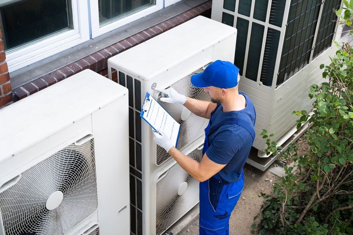 A person is holding a pressure gauge in front of a row of air conditioners.