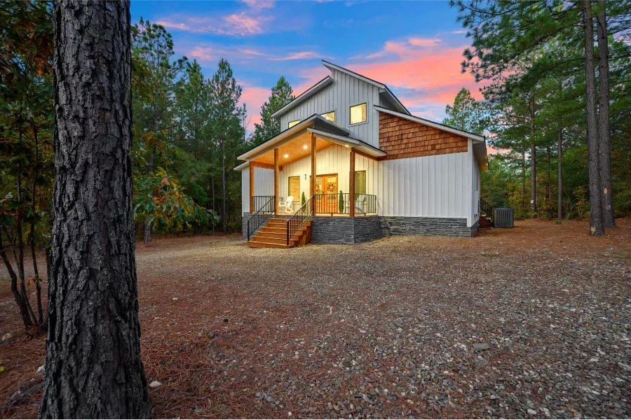 A white house with a porch in the middle of a forest.