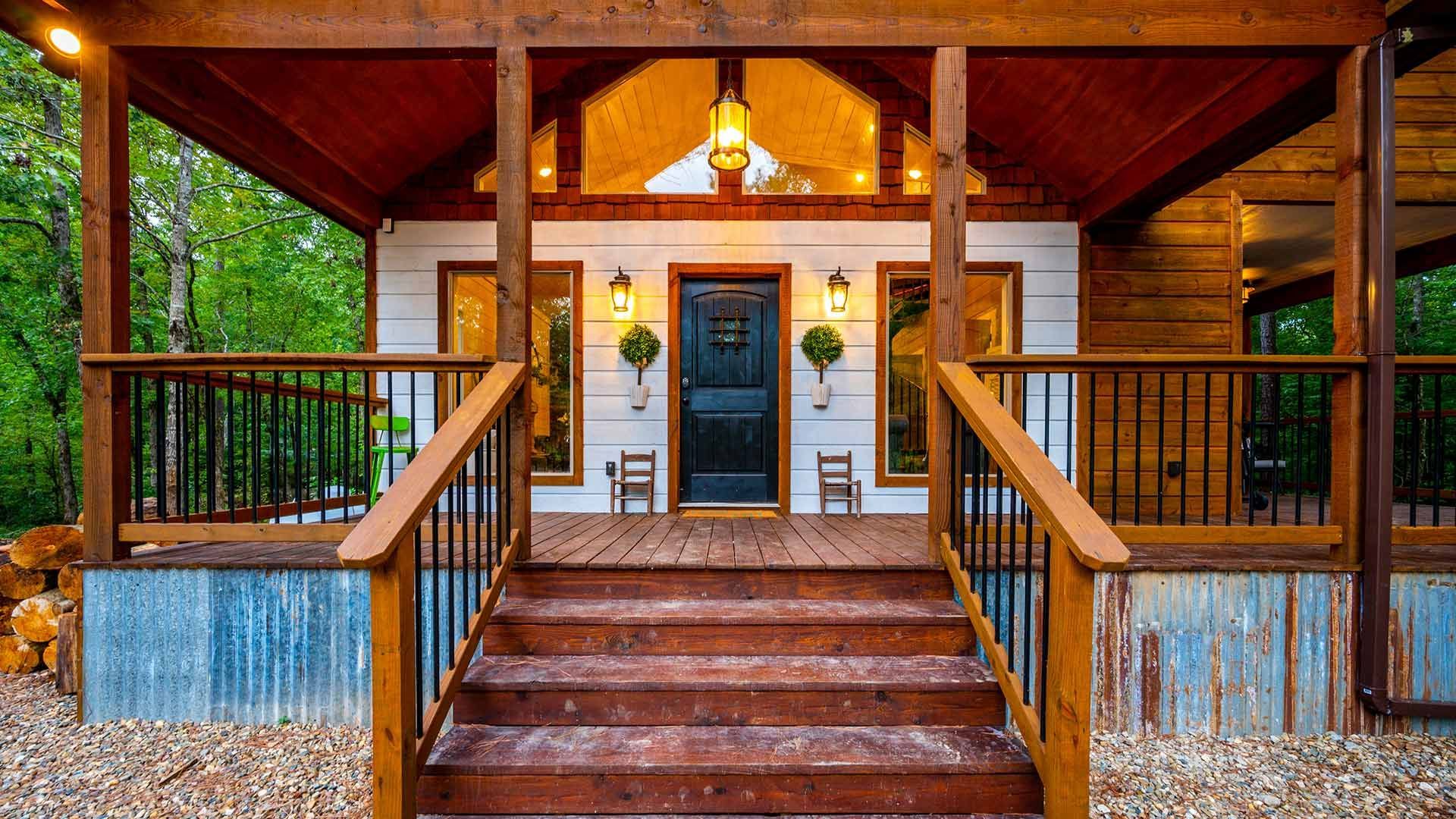 A front view of a rustic cabin entrance featuring a wooden porch, central black door, and corrugated metal base.