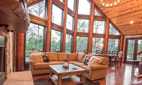 A living room with a couch , coffee table , fireplace and lots of windows.