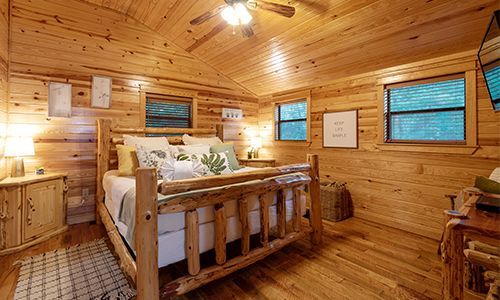 A bedroom in a log cabin with a bed and a ceiling fan.