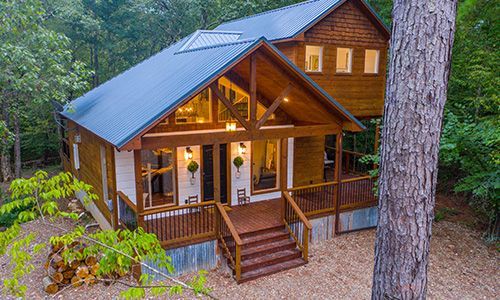 An aerial view of a log cabin in the middle of a forest.
