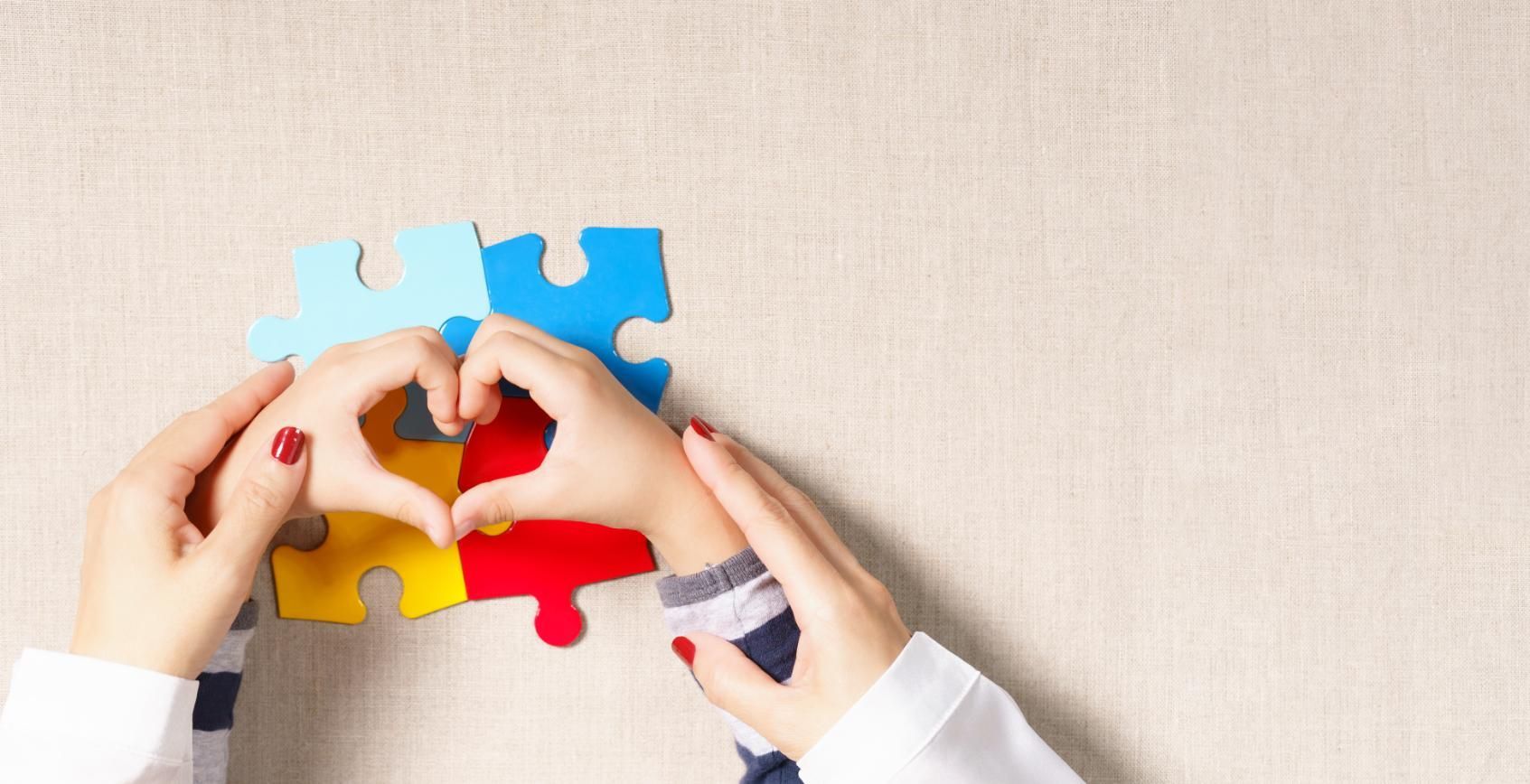 Hands fitting colorful puzzle pieces together on a light surface
