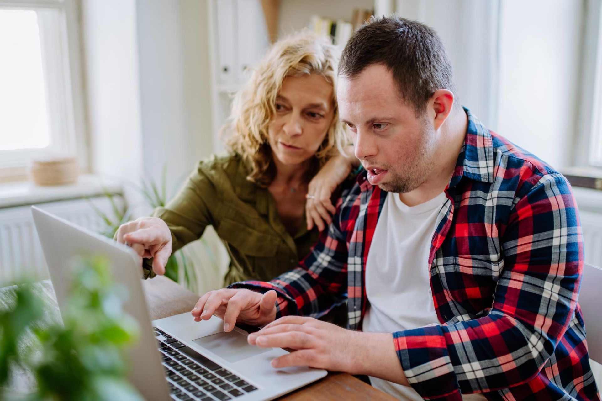 Two people leaning over a laptop and discussing something on the screen in a bright room