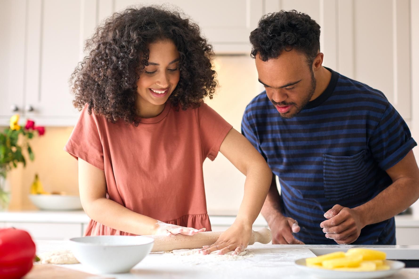 Two people kneading dough together in a bright kitchen