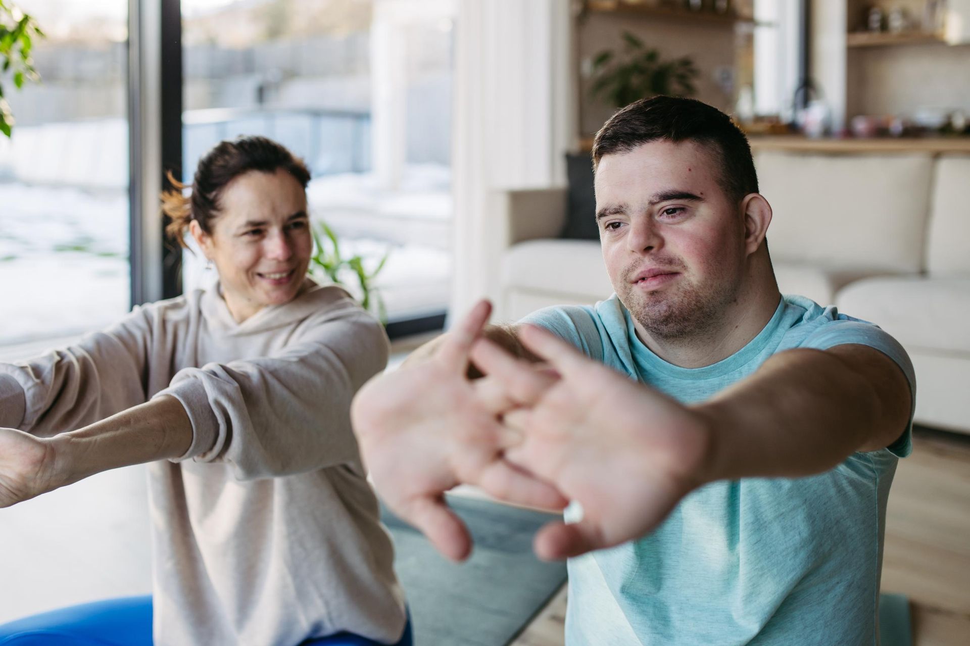 Two people stretching arms forward in a bright room, one smiling and one focused