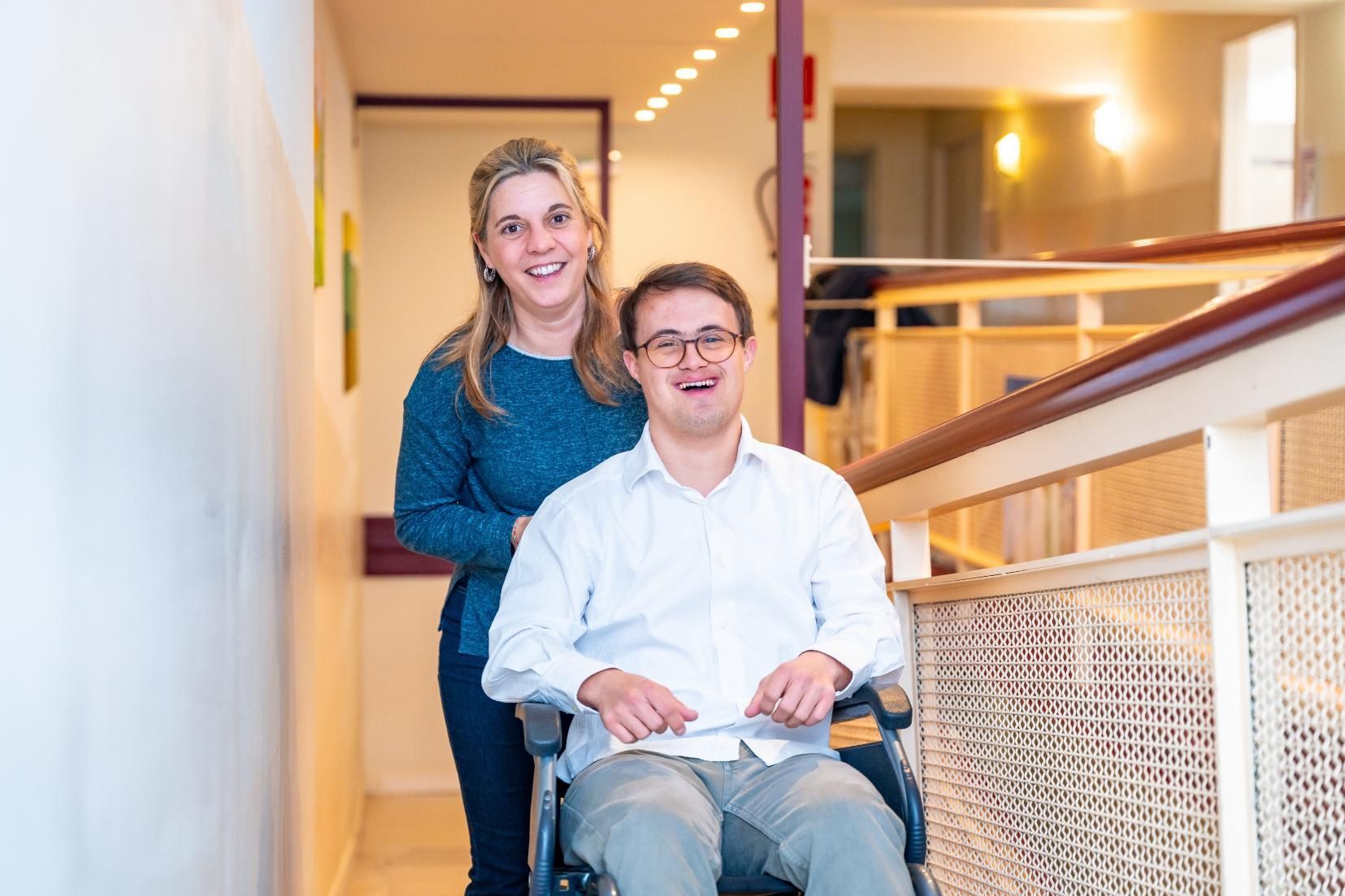 Woman pushing man in wheelchair down a bright hallway