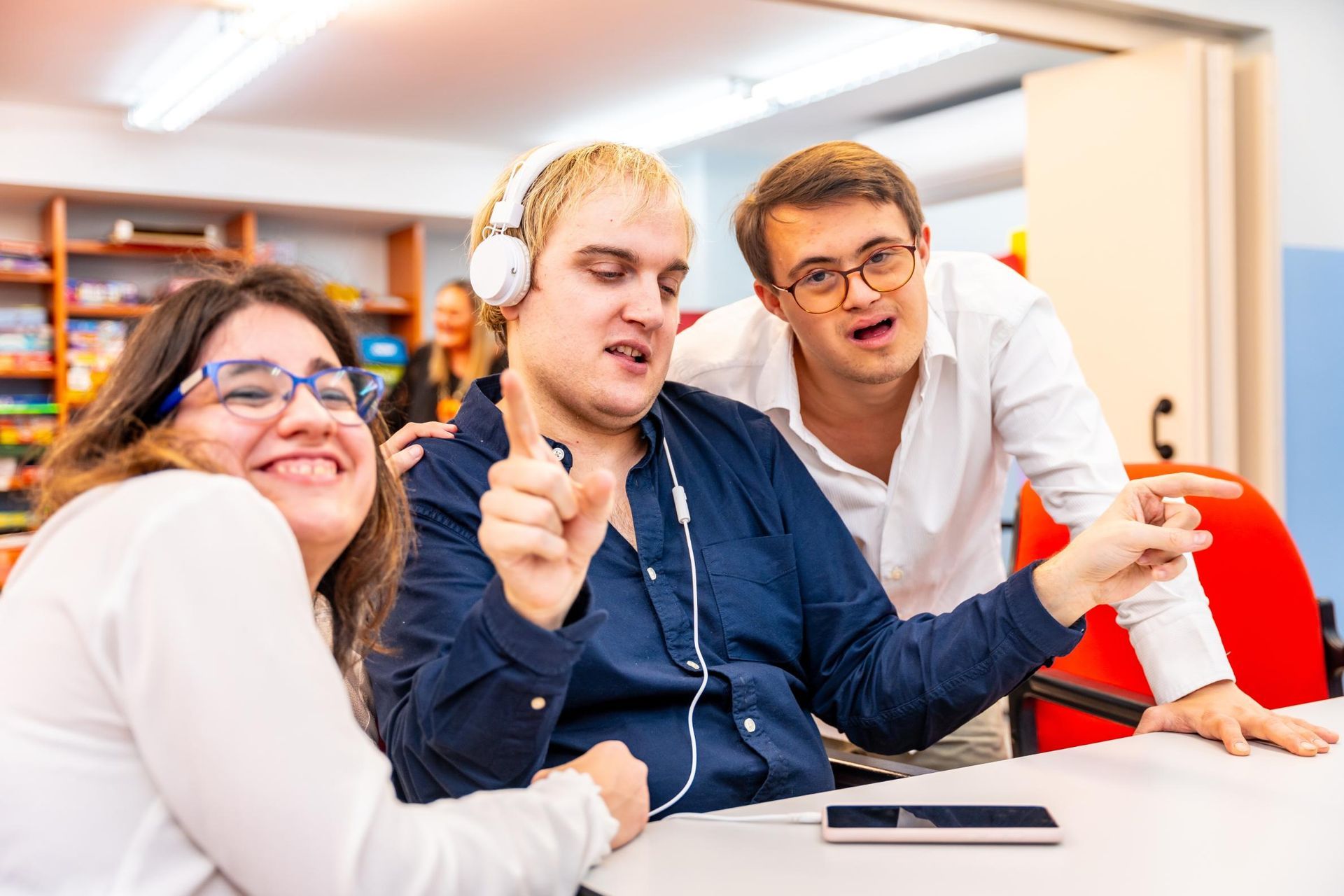 Three people in a bright office smiling and working together at a table with laptops and headphones