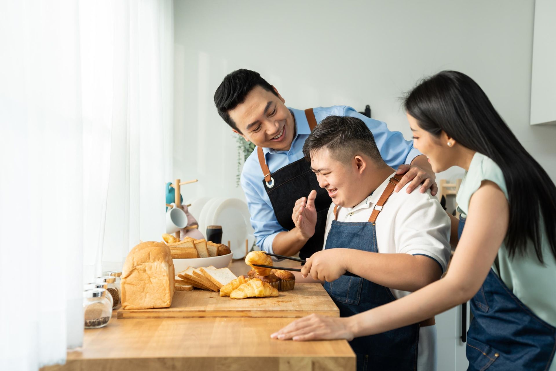 Three people baking bread together at a kitchen counter, smiling and cutting fresh loaves.