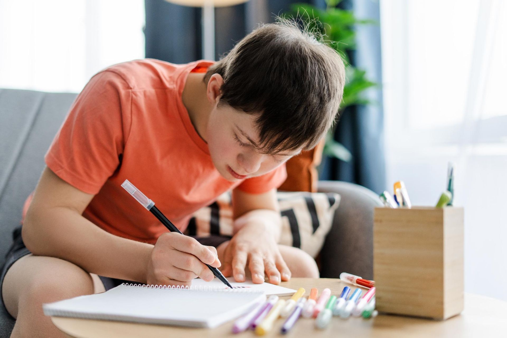 Child drawing on paper at a table with colored pencils and a wooden pencil holder