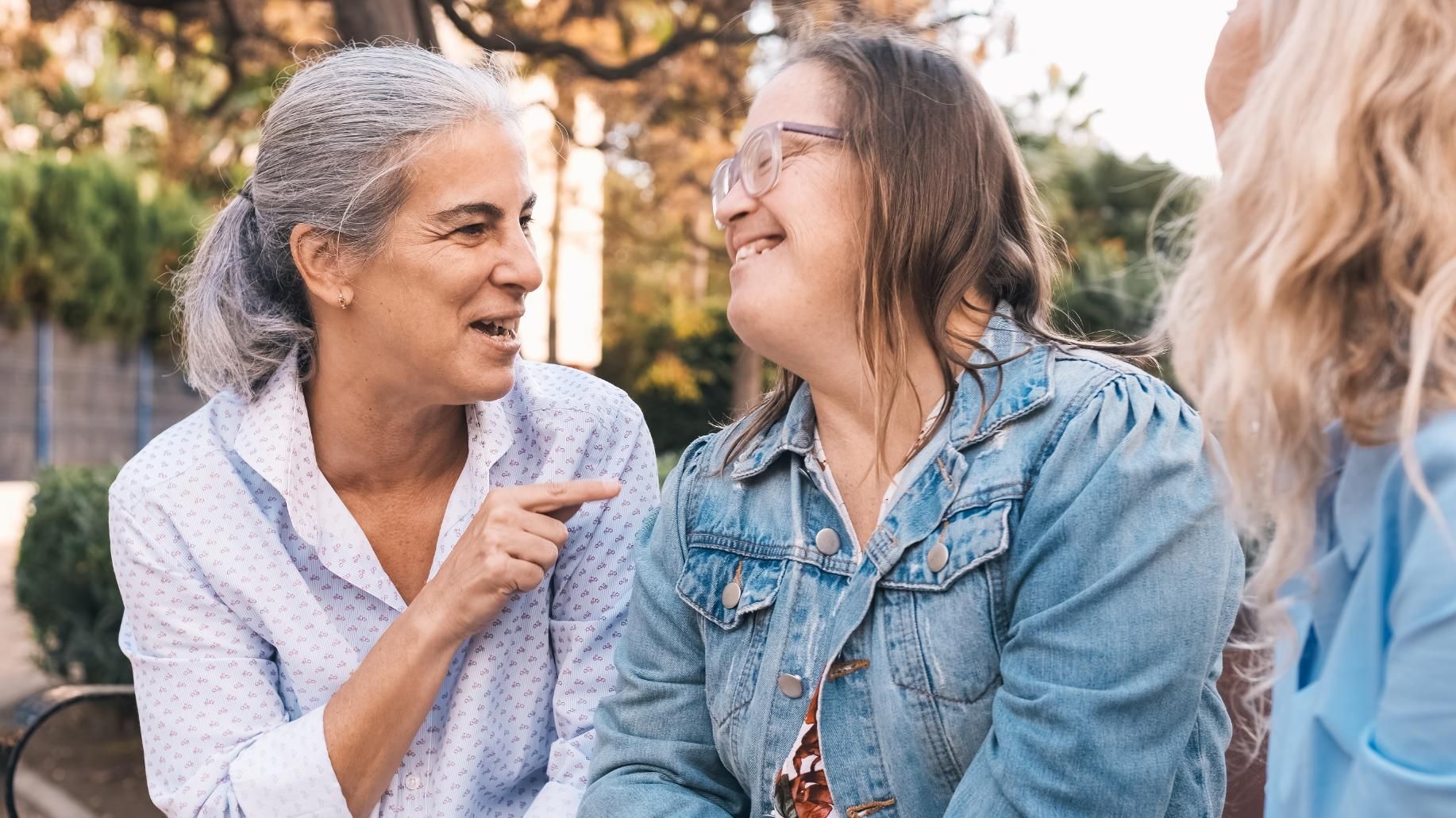 Two people smiling and talking outdoors, one in a denim jacket