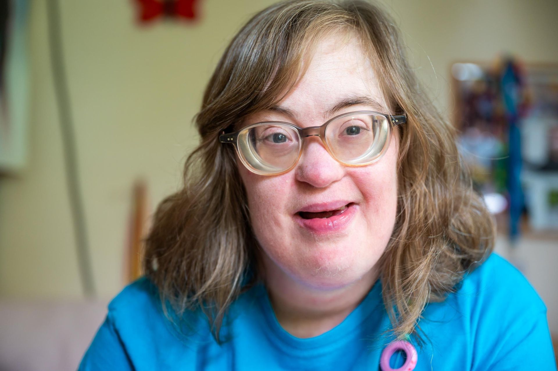 Smiling person wearing glasses and a blue shirt, seated indoors