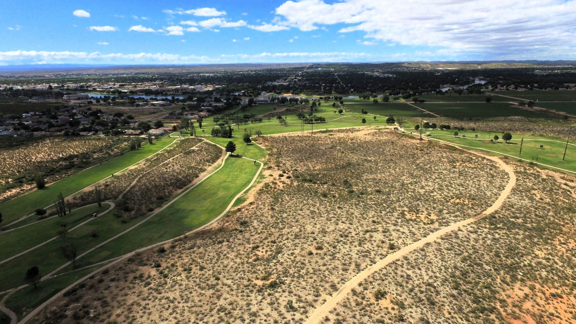 Person in red shirt swings golf club on a sunny driving range. Others watch.