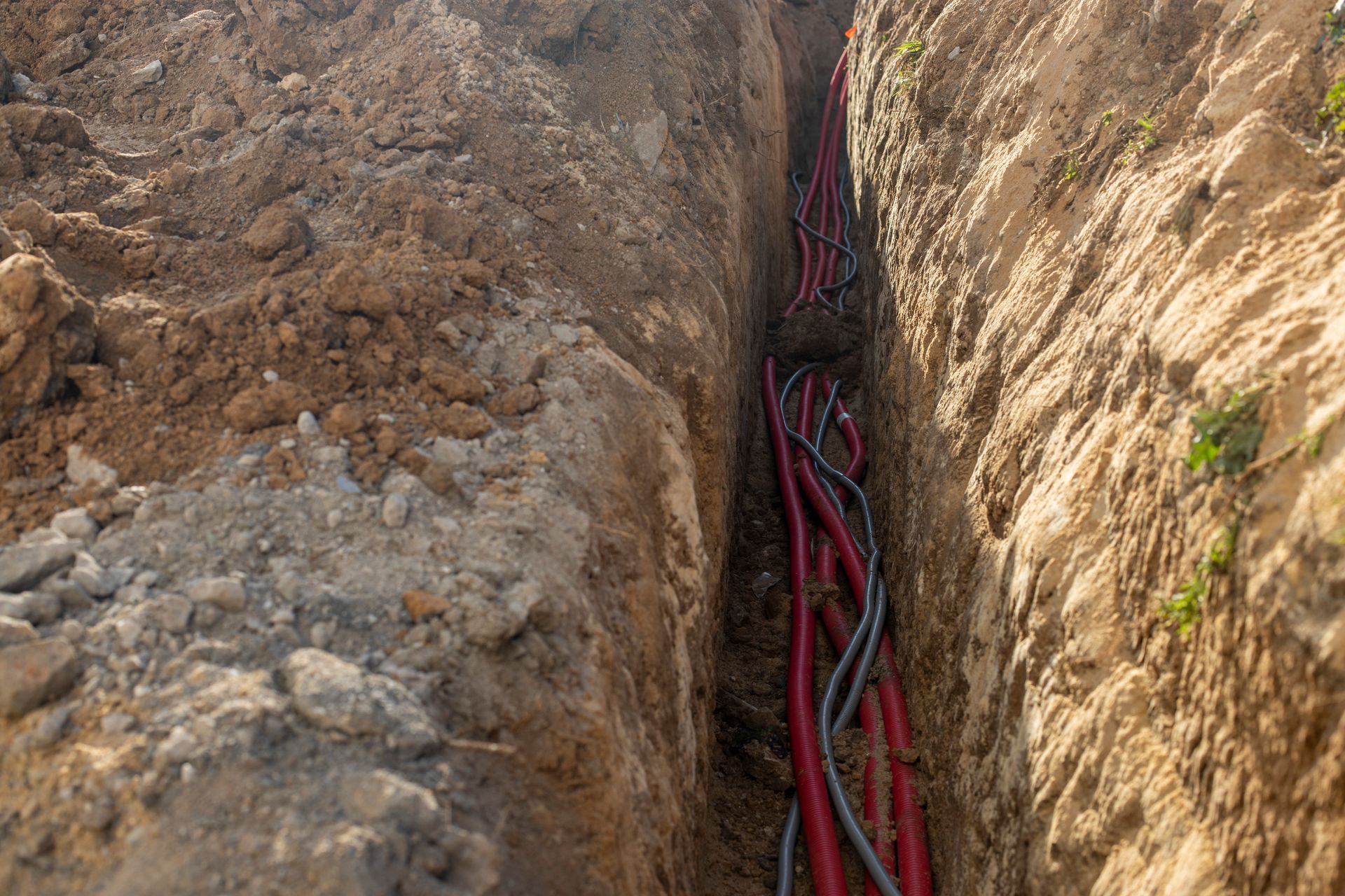 Red and black cables running through a narrow trench between dirt walls