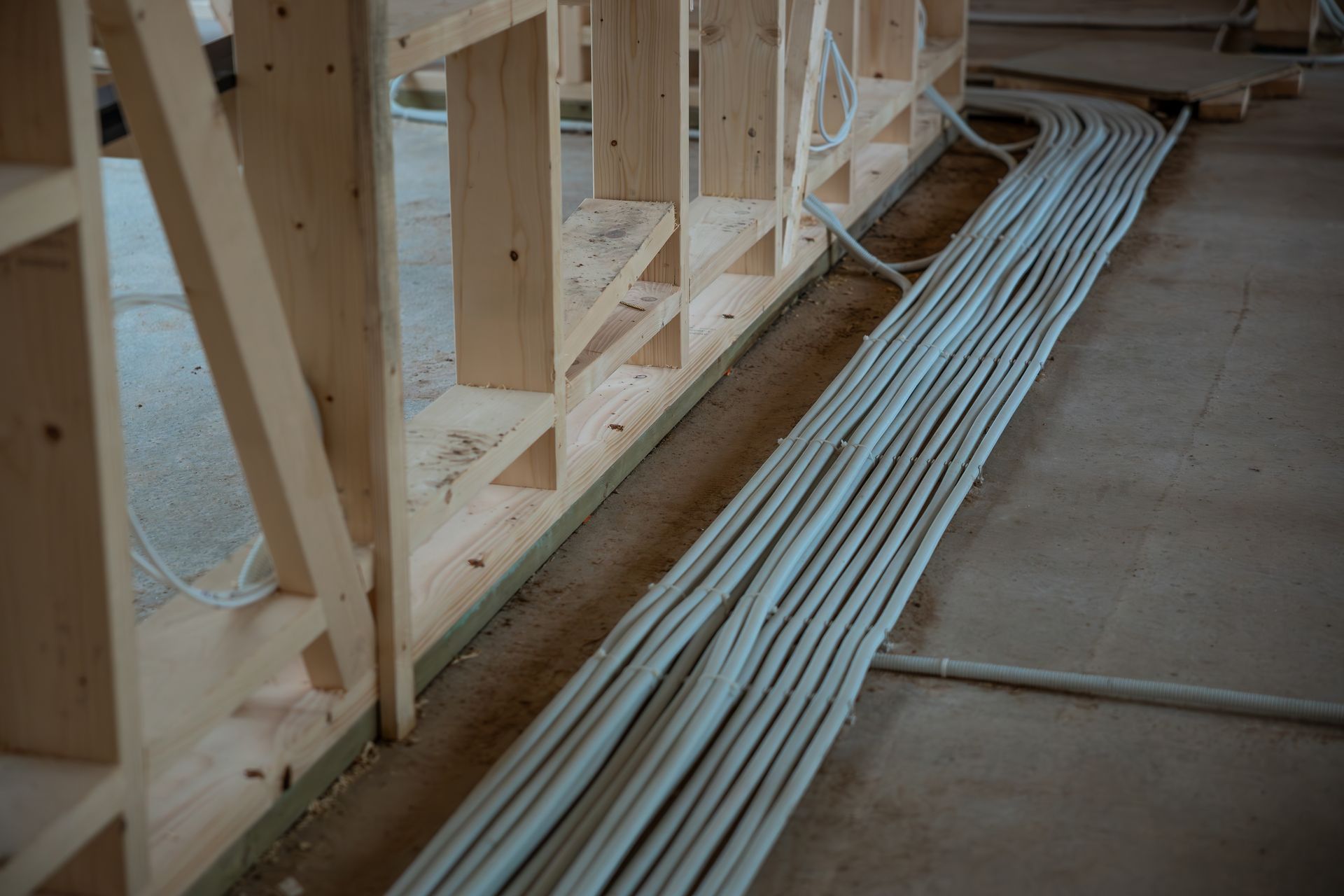 Wood framing under construction with bundled white electrical cables running along the floor.