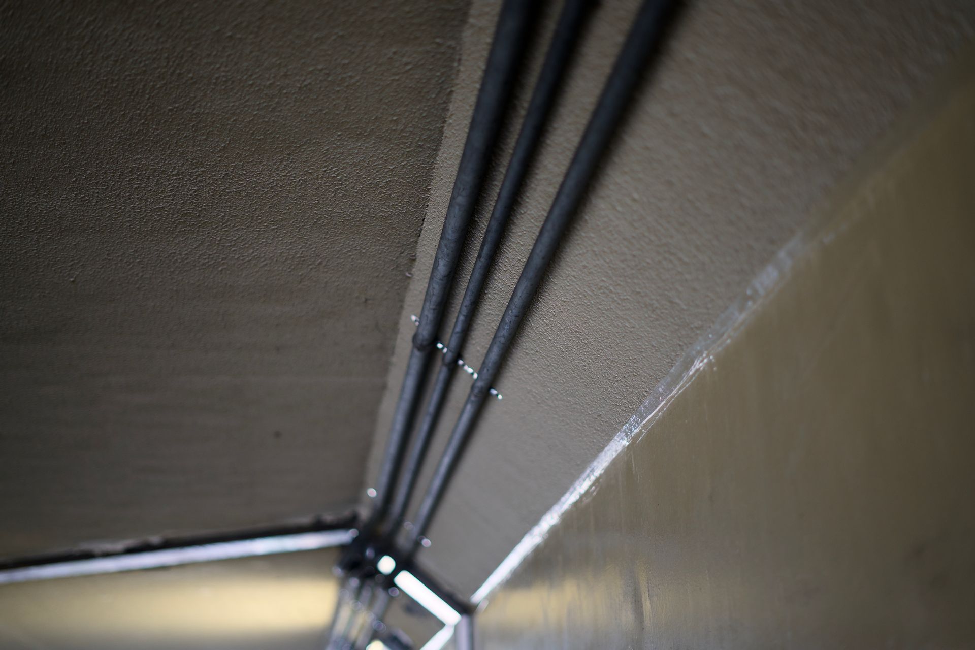 Close-up of a narrow ceiling corner with exposed black cables running along a beige wall.