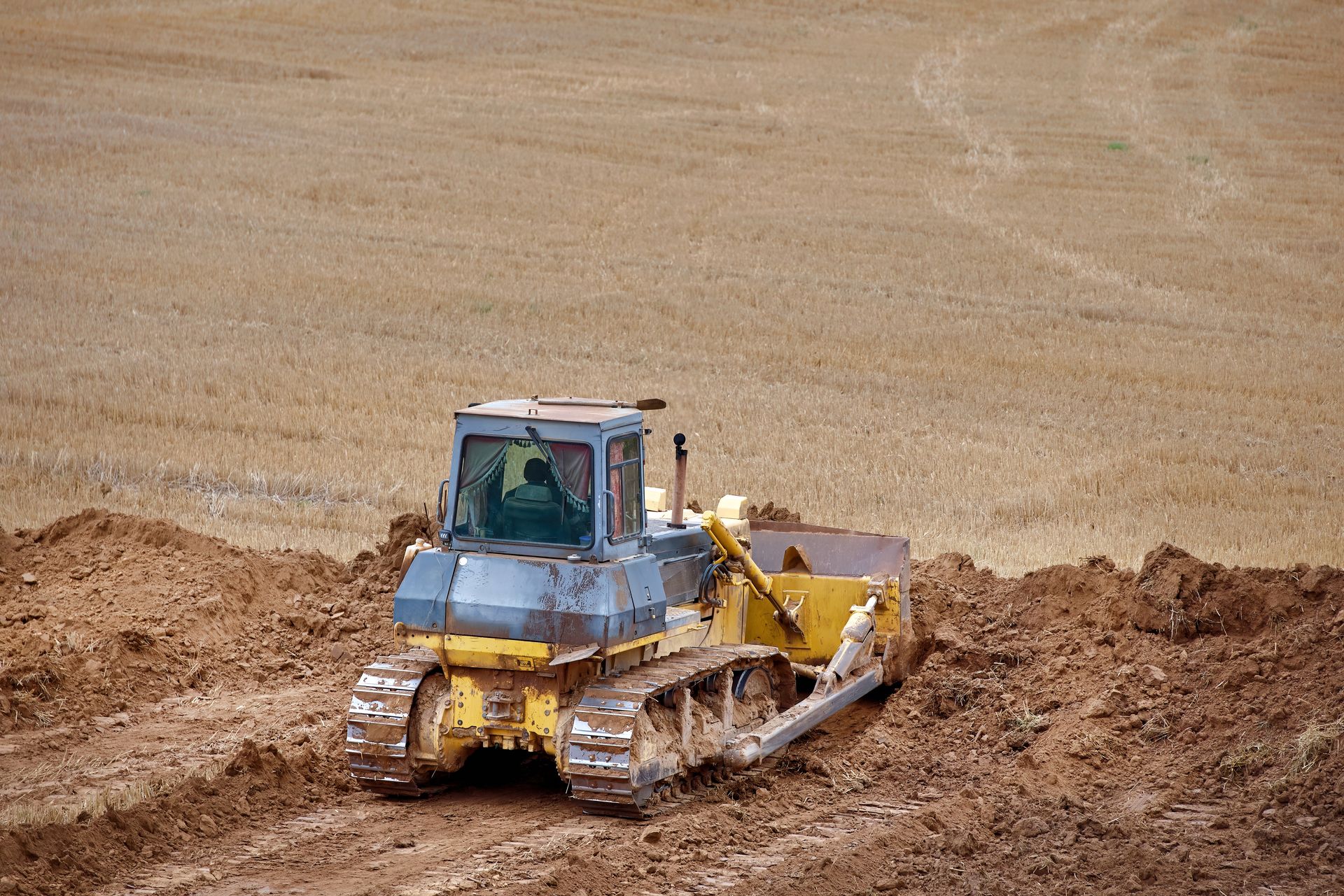 Yellow bulldozer pushing soil in a large dirt field