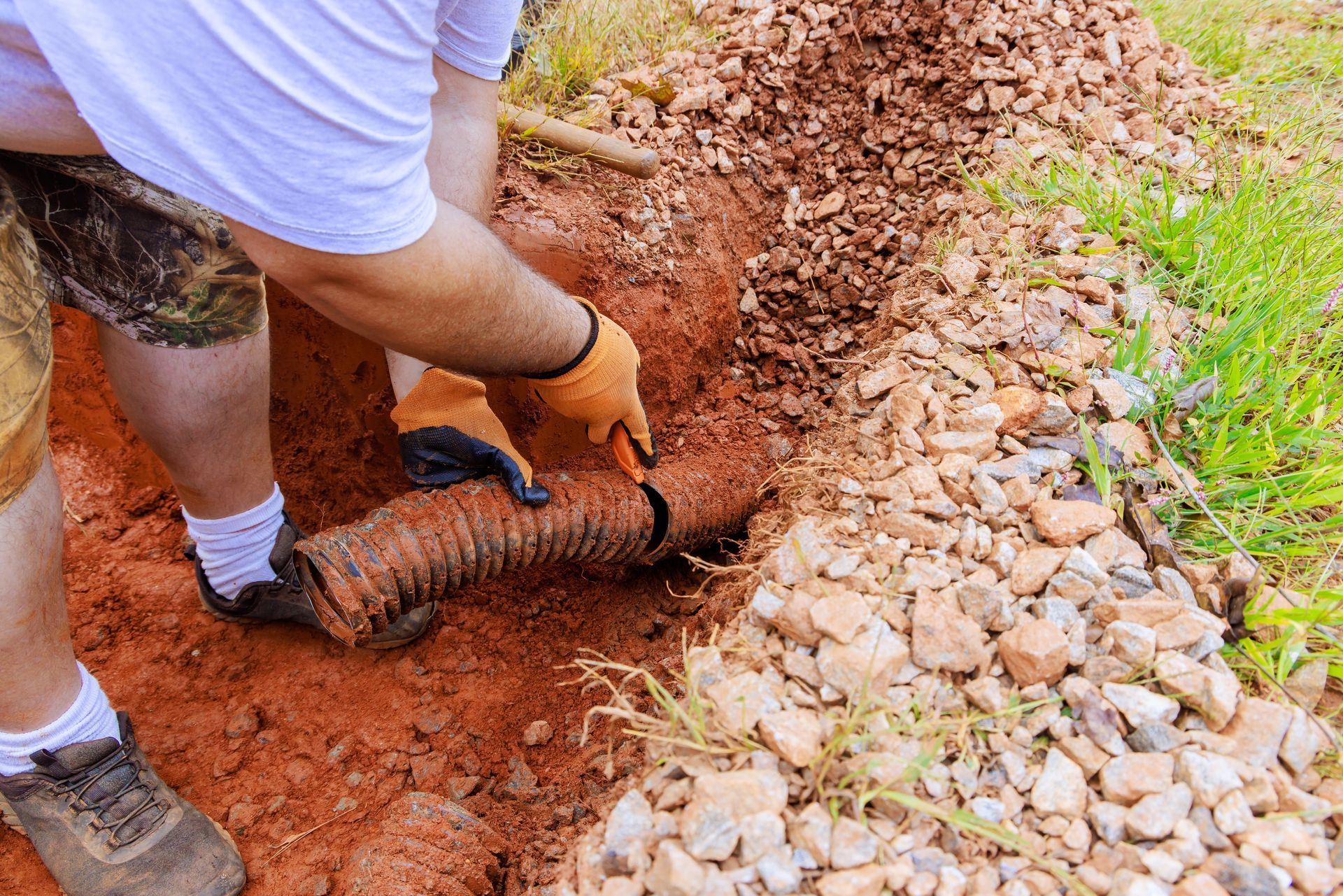 Worker compacting red soil along a stone border beside a grassy path