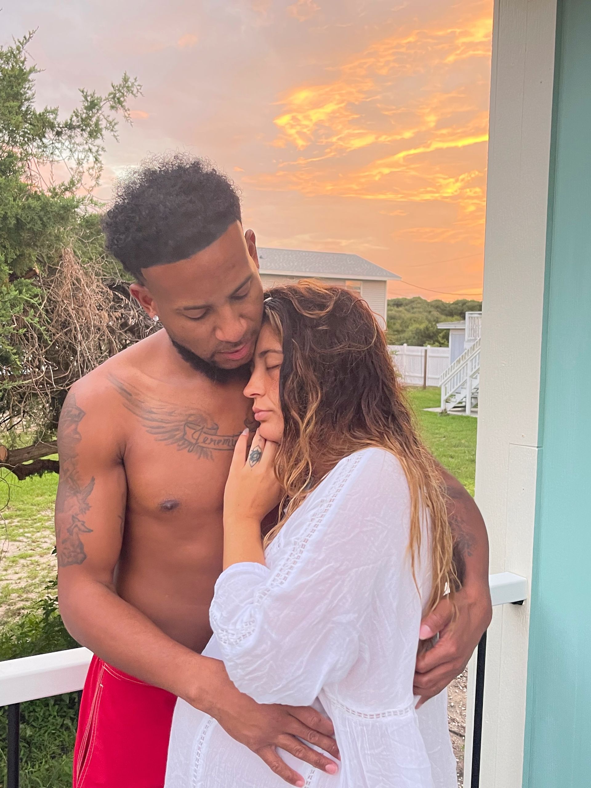 Couple embracing on a porch at sunset, with a warm orange sky and green yard in the background.