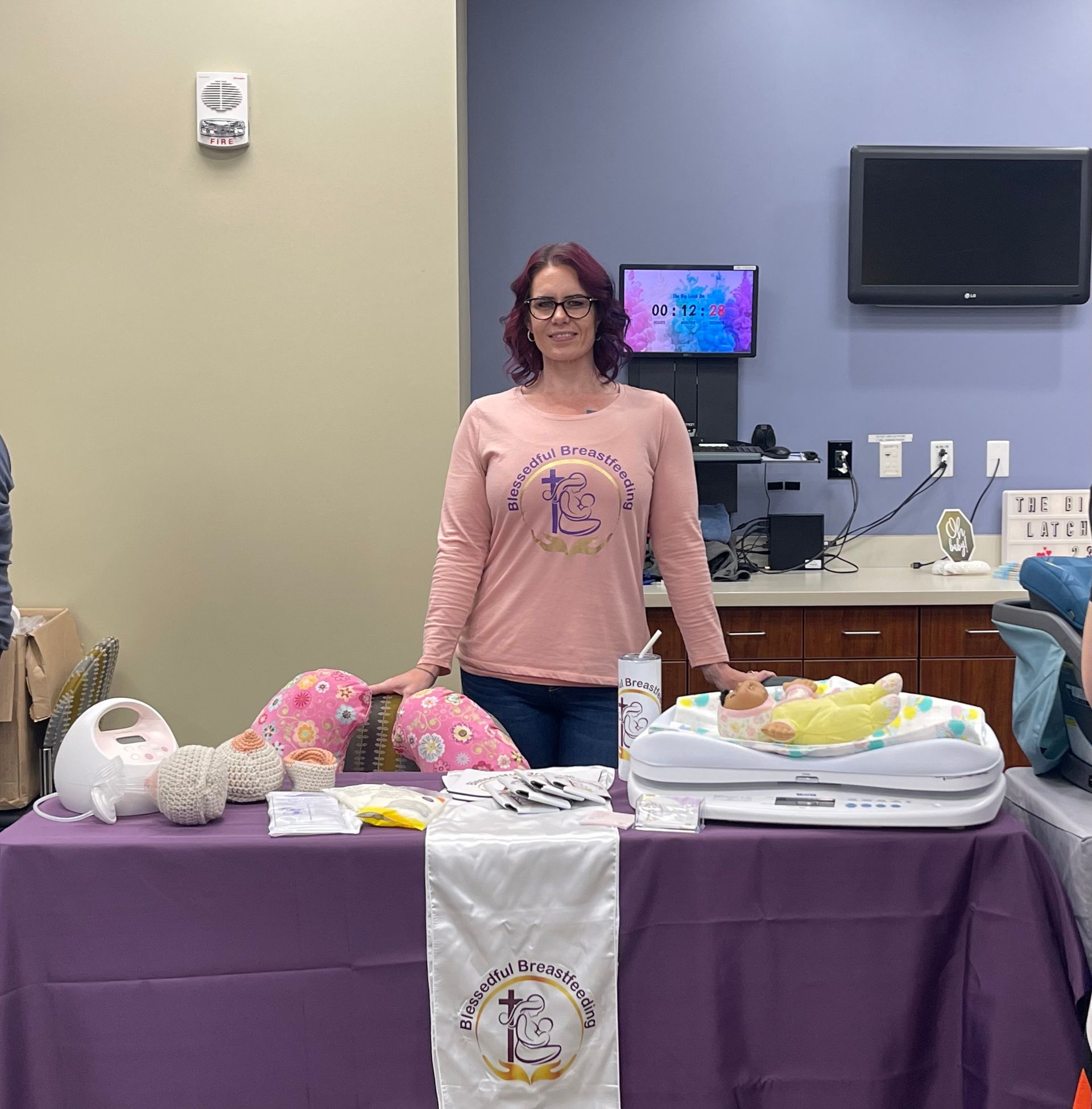 Woman behind a purple-draped table displaying gift baskets in a community room