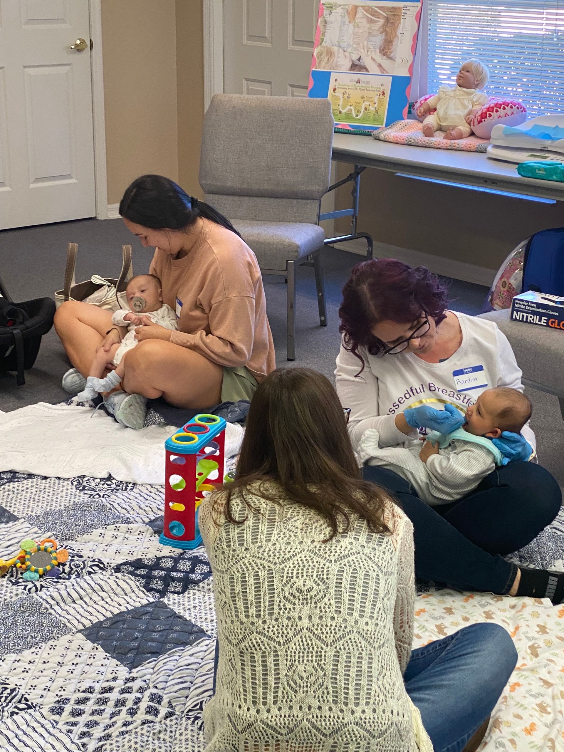 People sitting on the floor gently petting small dogs in a room with chairs and toys.