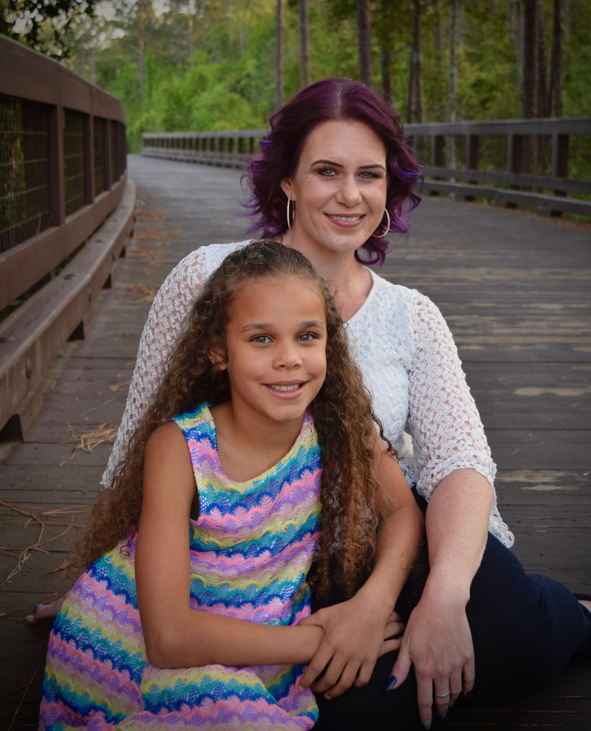 Woman and child sitting on a wooden bridge, smiling at the camera.