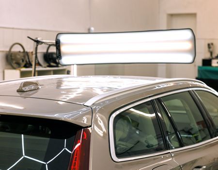Silver SUV in a workshop under bright overhead lights, with the rear and roof visible.