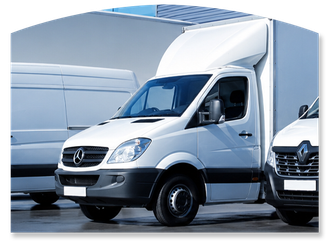 White delivery van parked beside a larger white truck in a warehouse yard